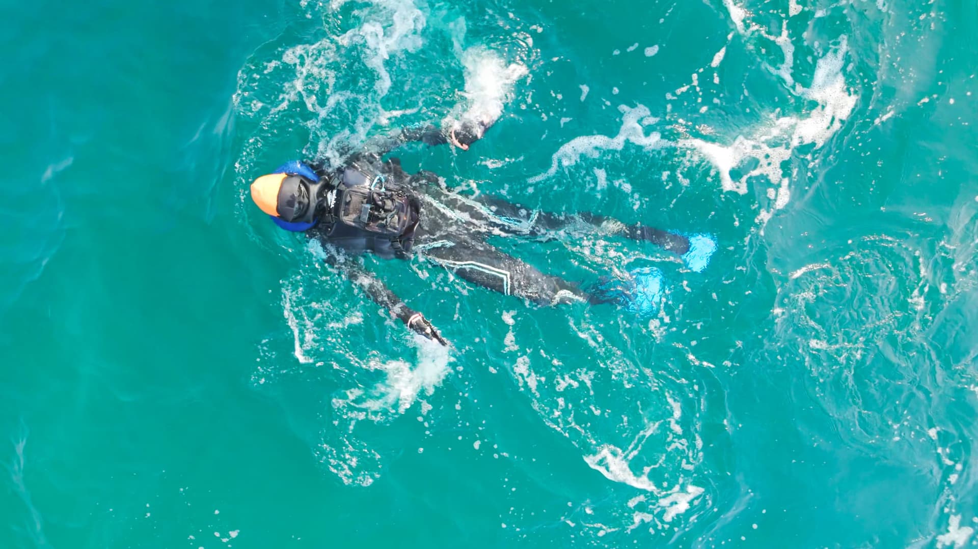 Aerial view of Karl Bushby swimming the Caspian Sea in a wetsuit, alone in turquoise open water.