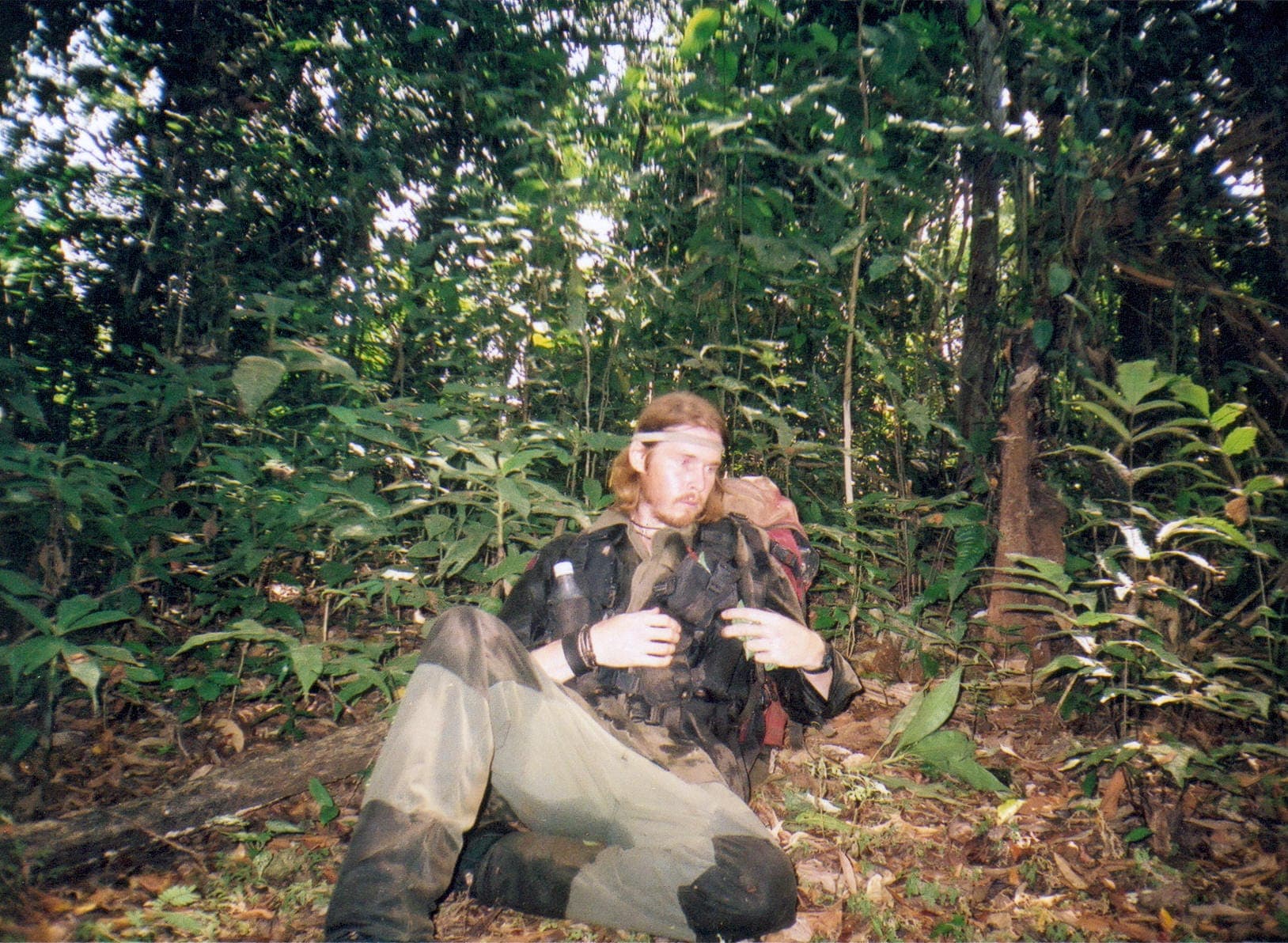 Karl Bushby resting on the jungle floor in the Darién Gap, mud-caked and exhausted, dense rainforest around him.