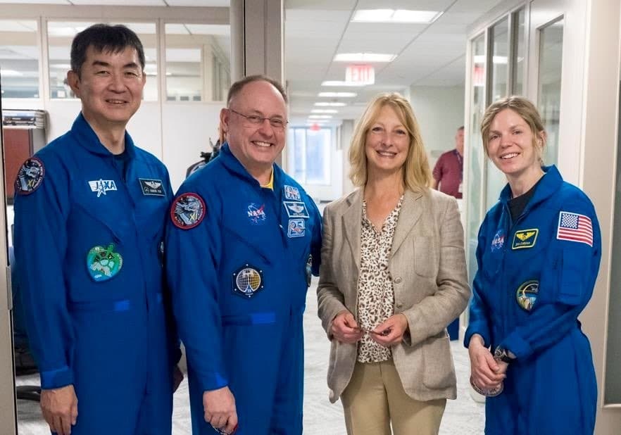 Mary Williams standing with three people in blue flight suits.
